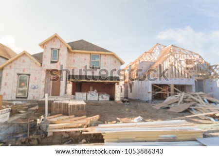Blurred abstract row of wood frame house under construction in suburban Irving, Texas, USA. New stick built 2 floor and almost completed home wall covered by panels, sheathing, envelope sealing Royalty-Free Stock Photo #1053886343