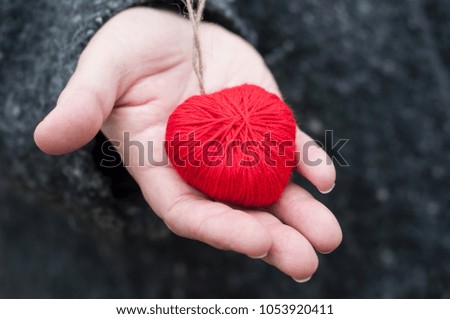 closeup of red woolen heart in hand of woman in outdoor 