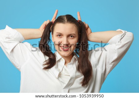 woman on blue background show horns looking at camera, smiling
