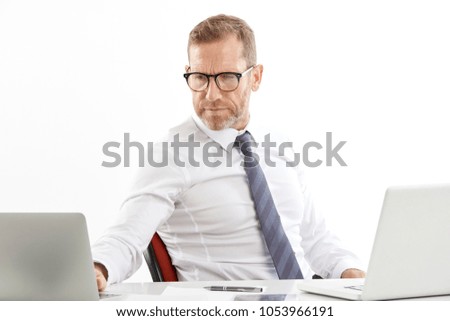 Stressed middle aged businessman sitting at office desk and working on computers. Isolated on white background. 