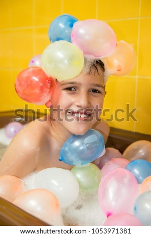 Young boy smiling, lying in a bathtub full of foam and colorful balloons  