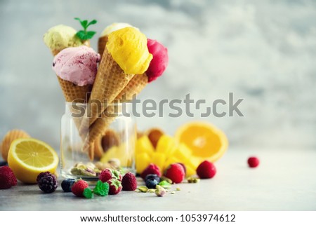 Colorful ice cream balls in waffle cones with different flavors - mango, lime, mint, pistachio, orange, strawberries, raspberries, blueberries. Summer concept.