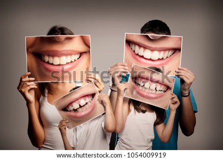 young family with children holding a picture of a mouth smiling on a gray background Royalty-Free Stock Photo #1054009919