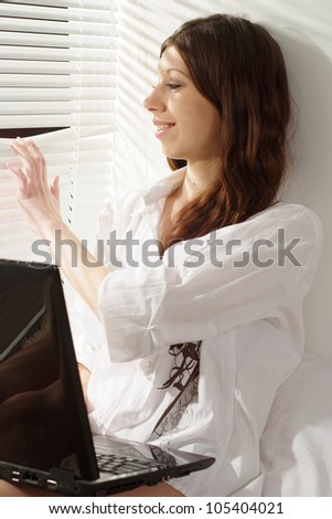 A happy caucasian female sitting on the carpet with a notebook against the window