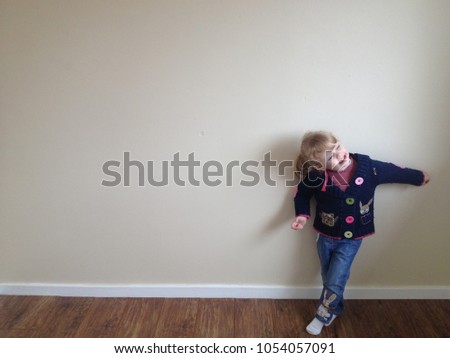 Gateshead, UK, March 30 2013: Barefoot 4 year old blonde girl playing dress up and dancing in front of beige room wall with brown wooden floor white skirting board. Patchwork knit cardigan girl