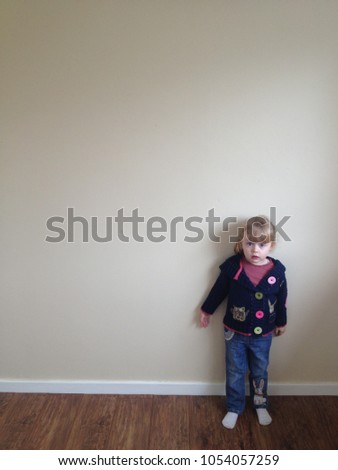 Gateshead, UK, March 30 2013: Barefoot 4 year old blonde girl playing dress up and dancing in front of beige room wall with brown wooden floor white skirting board. Patchwork knit cardigan girl
