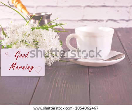Ã?up of coffee and a bouquet of white flowers on a table and with a card the inscription is a good morning