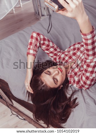young attractive girl with black hair in a red checkered shirt photographes herself on the camera lying on the bed
