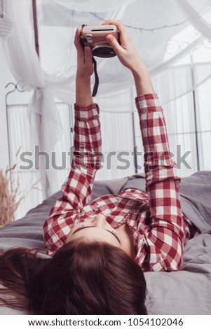 young attractive girl with black hair in a red checkered shirt photographes herself on the camera lying on the bed
