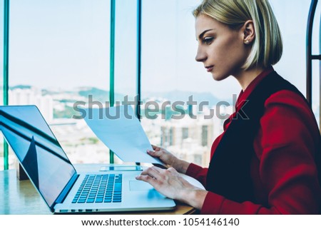 Serious experienced businesswoman working on laptop computer preparing financial report, side view of female executive manager checking information from database on netbook holding blank papers