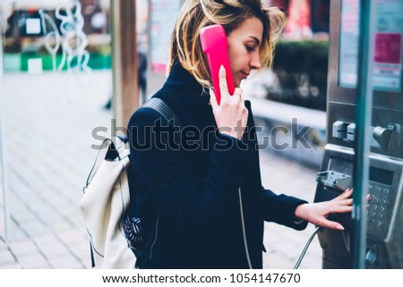 Young female traveler using old fashioned public telephone for making international calls on trip, pensive hipster girl dialing number on metal payphone operated with coins for having conversation Royalty-Free Stock Photo #1054147670