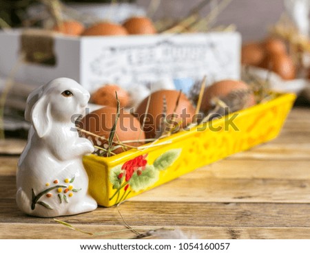 Porcelain Easter white bunny with colorful eggs on wooden background, selective focus
