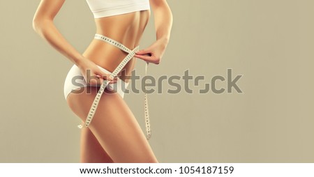  Perfect slim toned young body of the girl . An example of sports , fitness or plastic surgery and aesthetic cosmetology.Woman measuring her waist over white background Royalty-Free Stock Photo #1054187159