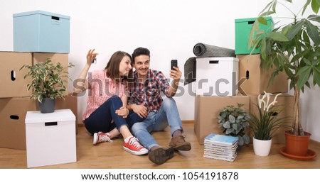 Happy Couple Showing New Home Keys to Family while Talking on Mobile Phone in a Video Conference Call in Apartment Living Room