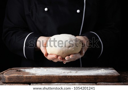 Female chef holding yeast dough in her hands on black background