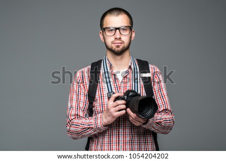 Young bearded traveler man with camera on gray background