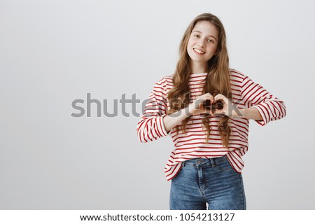 Showing what you mean to her. Cute young woman in casual outfit making heard gesture over chest and smiling cheerfully, thanking dear friend for help, showing affection and love over gray background