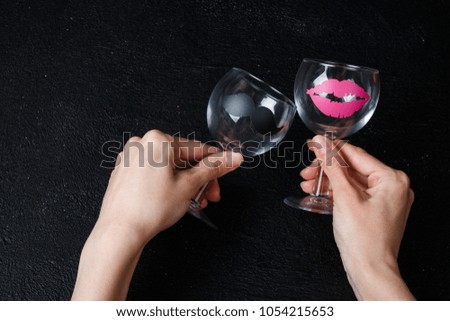 Wine glasses with stickers in the form of female lips and man's mustache in hands on a black background