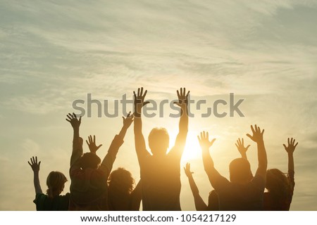 People silhouette at sunset. Happy fans of a rock group outdoor. Human body over natural colorful sky background.
