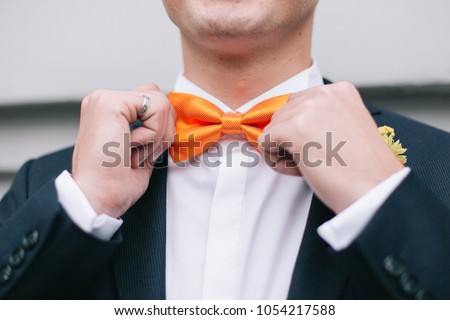The groom in a suit touch up a bright orange bow tie. Special ocassion