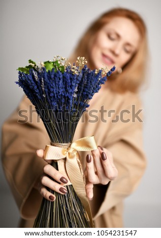 Beautiful red hair woman wearing brown yellow designers dress coat and bouquet of blue flowers lavender on white background