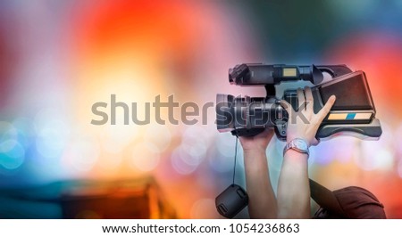 Video camera operator working with his equipment. Cameraman lifts the camcorder above his head while filming video with colorful light 