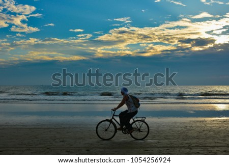 A woman riding a bike along the coastline on Arambol beach on the background of a beautiful sunset in North Goa.India