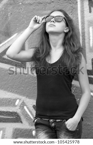 Style teen girl in sunglasses near graffiti background. Photo in black and white style.