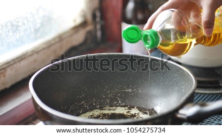 Woman’s hand is holding the oil of bottle and pouring oil onto the teflon pan for cooking food. The teflon pan is corrosive and harmful to health. The picture concepts are food, healthy, cancer, fat.