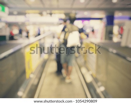 Abstract blurred image background of group people or arriving passengers with their suitcases and luggage rushing through an escalator in international airport terminal, travelling or business concept