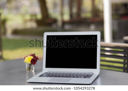 Blank screen laptop on wooden table blurred garden in home background.