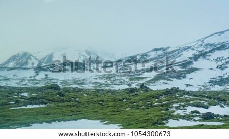 Iceland extreme bad weather snow and fog mountaitn background, green moss field