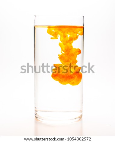 Orange food coloring diffuse in water inside cylinder glass with empty copy space area for slogan or advertising text message, over isolated white background.