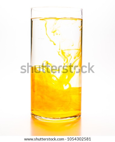 Orange food coloring diffuse in water inside cylinder glass with empty copy space area for slogan or advertising text message, over isolated white background.