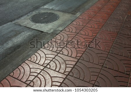 Curve brick footpath Pattern Sidewalk with Circle rusty iron manhole cover on road floor Yaowarat rd, Bangkok, Thailand 