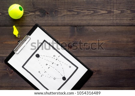 Sport coach concept. Pad with tactic plan of the match near whistle and tennis ball on wooden background top view copy space