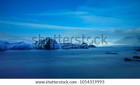 Long Exposure photography of blue iceberg floating in front of white large glacier at Jokulsalon glacial lagoon, Iceland                               