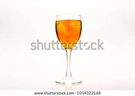 Orange food coloring diffuse in water inside wine glass with empty copy-space area for slogan or advertising text message, over isolated white background.