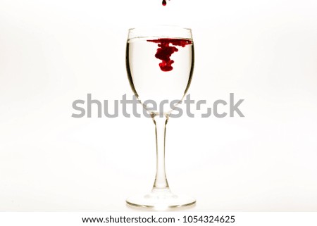 Red food coloring diffuse in water inside wine glass with empty copy-space area for slogan or advertising text message, over isolated white background.