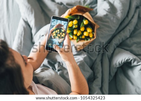 woman take picture of bouquet of yellow tulips. romantic surprise in bed