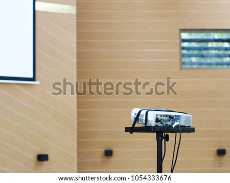 high power overhead projector on a stand inside educational or business conference hall with modern interior decoration wall and hanging white display ready setup for seminar and lecture hour 
