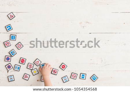 Top view on toddler's hand playing with toy road signs on white wooden table background. Learning traffic signs.