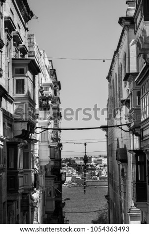 Typical narrow street leading to the sea on the island of Malta. Buildings with traditional colorful maltese balconies in historical part of Valletta. Black and white picture