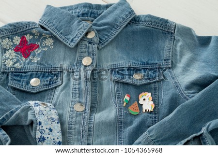 Close up view of denim girl jeans jacket with cool graphic pins, funky metallic brooch horse unicorn pegasus, fashion accessories