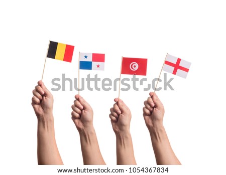 Little paper national flags in hands isolated on white background. Flags of national football teams of Belgium, Panama, Tunisia, England. World cup competitors in group G Royalty-Free Stock Photo #1054367834