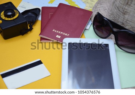 Traveler getting ready for a trip, he is packing his bag and booking a flight online using a credit card and a tablet. Travel accessories, passports, world map, hat, sunglasses.