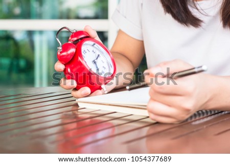Woman wear white shirts with ted alarm while trying to write the white paper on wood table in the vacation.