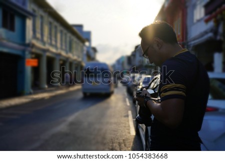 Asian male tourist look the photo on his camera with town background and sunlight.