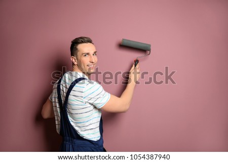 Young male decorator with paint roller near color wall