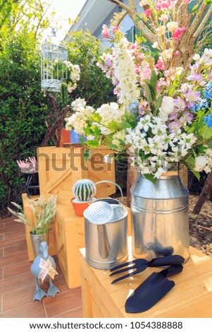 Beautiful flowers in metal vase and watering cans with swarm on wooden box and a cactus in a pot with a duck doll on wooden floor in backyard.